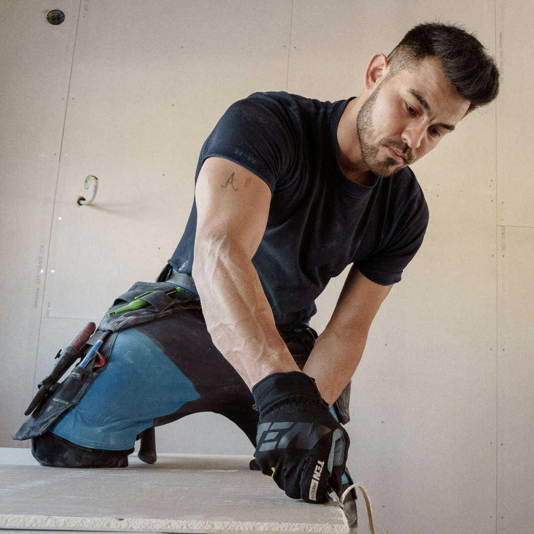 A construction worker cutting drywall with precision, wearing protective gloves and equipped with tools.