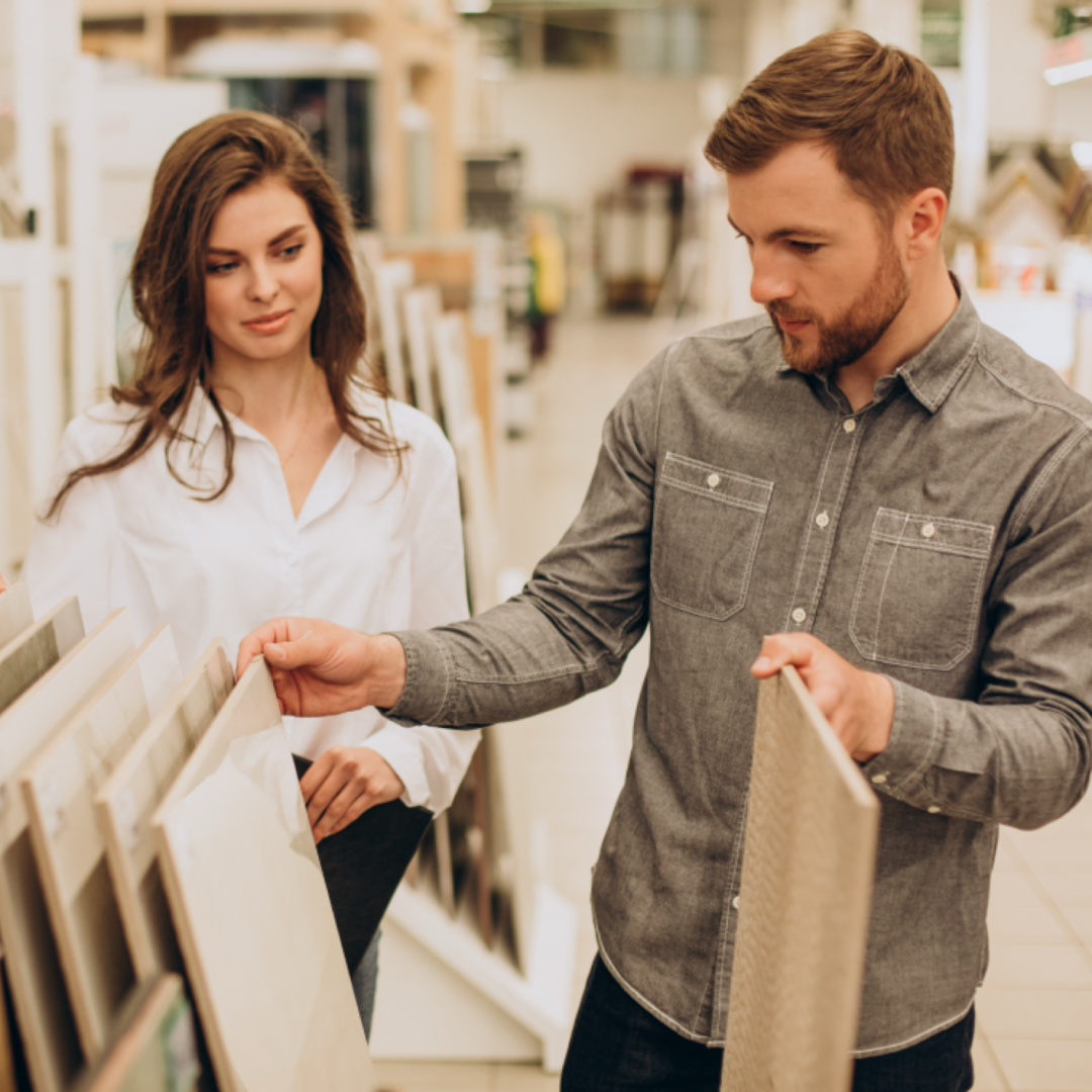 This image captures a couple in a home improvement store carefully reviewing tile samples. They are thoughtfully selecting materials that best suit their design preferences. The wide variety of tiles presented includes different colors, textures, and patterns, offering numerous options for their renovation project. The store’s setup provides a detailed view of available tile options, helping them make the perfect choice for their home.