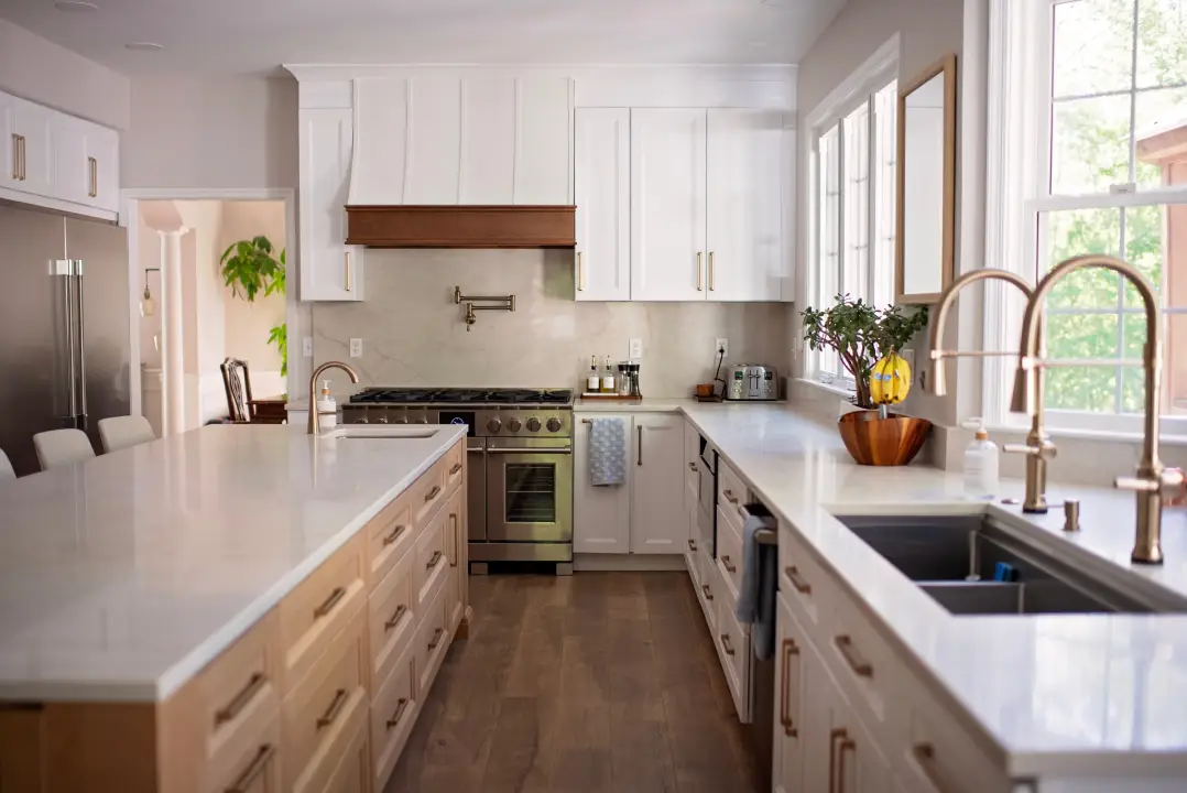 Modern kitchen with a large white island, light wood cabinets, and stainless steel appliances. Bright and inviting, with greenery by the window.