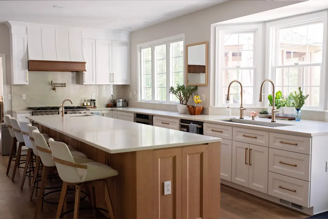 Modern kitchen with a large white island, light wood cabinets, and stainless steel appliances. Bright and inviting, with greenery by the window.