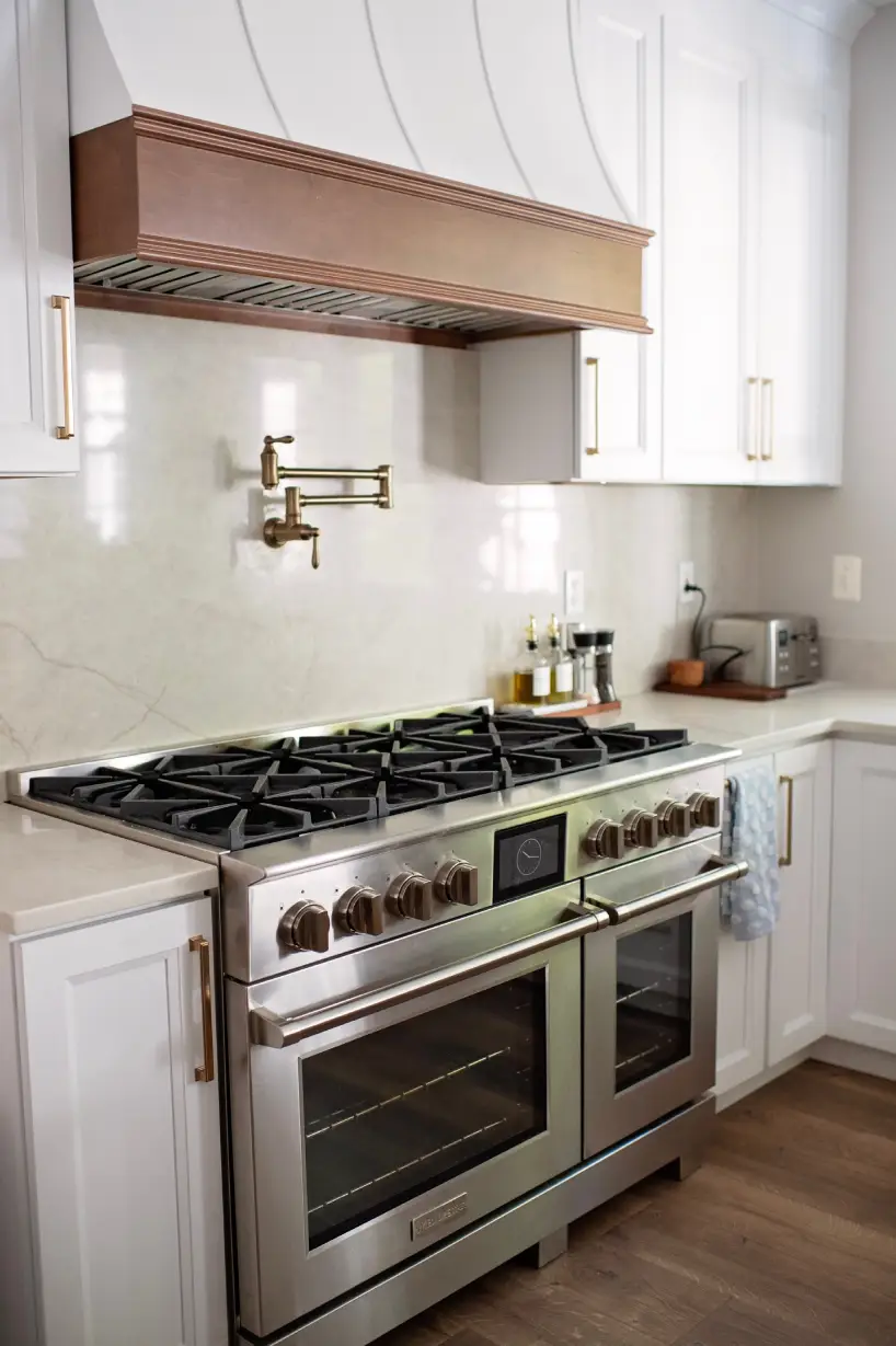 Modern kitchen with a stainless steel oven and stove. White cabinets and marble backsplash create a clean look. A pot filler and kitchenware add elegance.